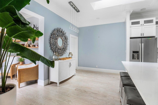 interior space with stainless steel refrigerator with ice dispenser, white cabinetry, ornamental molding, and a skylight