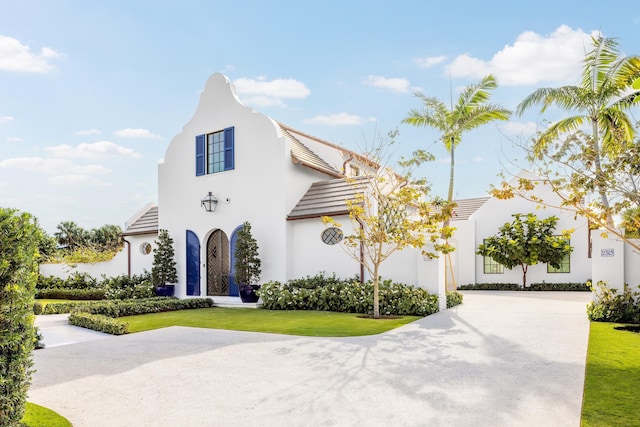 view of front of home featuring a tile roof, concrete driveway, a front lawn, and stucco siding