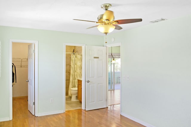 unfurnished bedroom featuring ceiling fan, ensuite bath, a closet, a walk in closet, and light hardwood / wood-style flooring