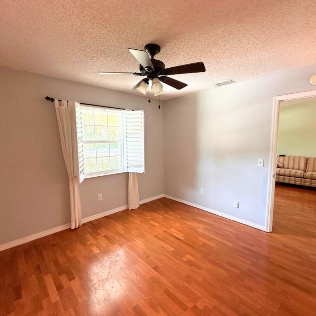 empty room with ceiling fan, wood-type flooring, and a textured ceiling