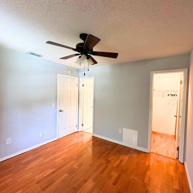 unfurnished bedroom with ceiling fan, a spacious closet, a textured ceiling, and hardwood / wood-style flooring