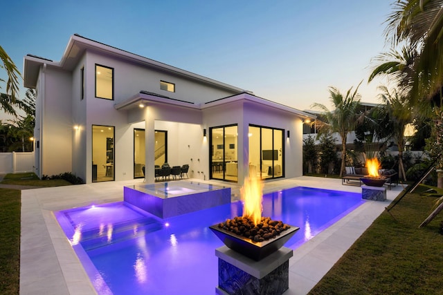 back house at dusk featuring a fire pit, a swimming pool with hot tub, and a patio