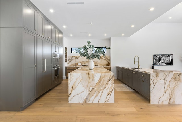 kitchen with sink, a large island, light stone counters, light hardwood / wood-style flooring, and gray cabinetry