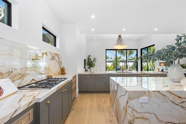 kitchen with light stone countertops, light wood-type flooring, stainless steel gas cooktop, and backsplash