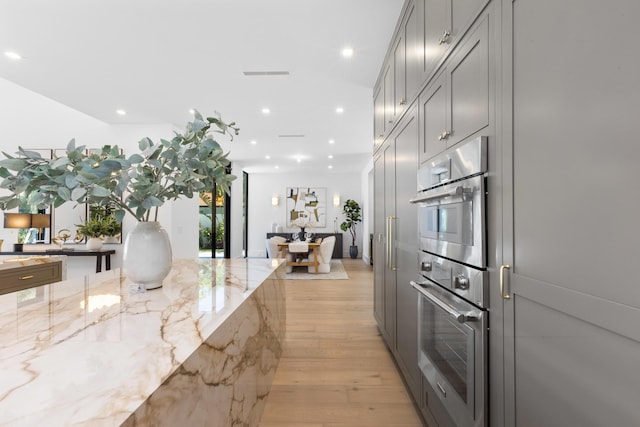 kitchen featuring double oven, light stone countertops, light wood-type flooring, and gray cabinets