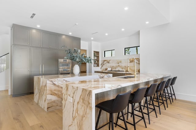 kitchen featuring sink, light stone counters, a kitchen bar, kitchen peninsula, and gray cabinetry