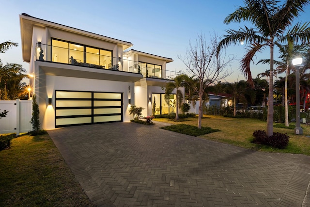 contemporary home featuring a balcony, a garage, and a lawn