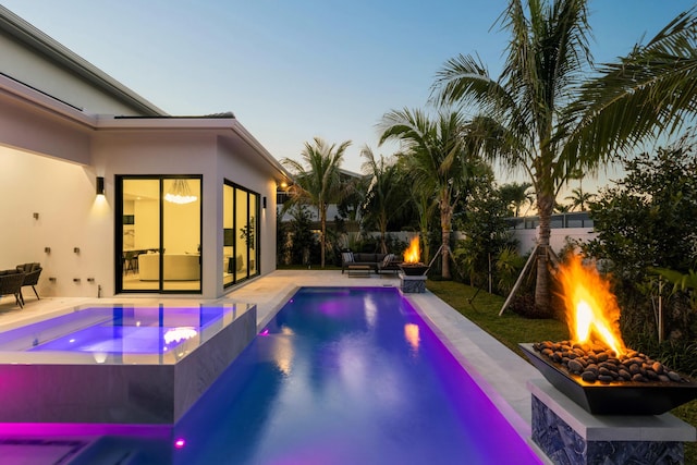 pool at dusk with a patio area, an in ground hot tub, and a fire pit