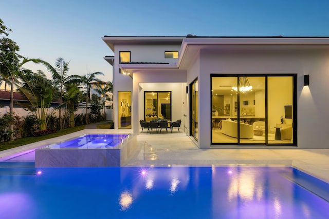 back house at dusk with a patio area and a swimming pool with hot tub