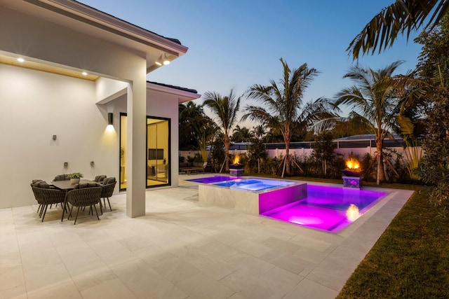 pool at dusk featuring a patio and an in ground hot tub