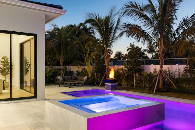 pool at dusk with an outdoor living space with a fire pit, a patio area, and an in ground hot tub