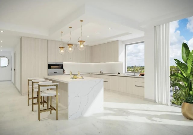 kitchen featuring light stone countertops, hanging light fixtures, a tray ceiling, and an island with sink