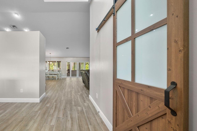 corridor featuring light hardwood / wood-style flooring, an inviting chandelier, and a barn door