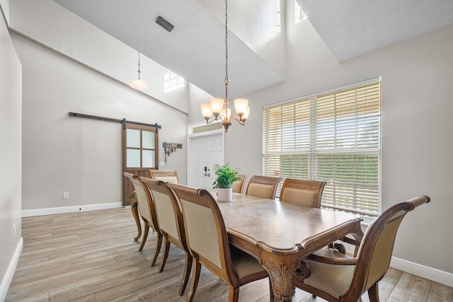 dining room with a high ceiling, a chandelier, light hardwood / wood-style floors, and a barn door