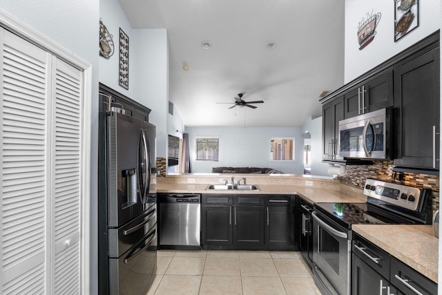 kitchen featuring light tile patterned floors, stainless steel appliances, backsplash, a sink, and dark cabinets