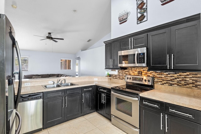 kitchen featuring stainless steel appliances, open floor plan, dark cabinetry, and a sink