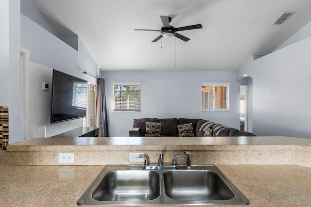 kitchen featuring lofted ceiling, visible vents, arched walkways, and a sink