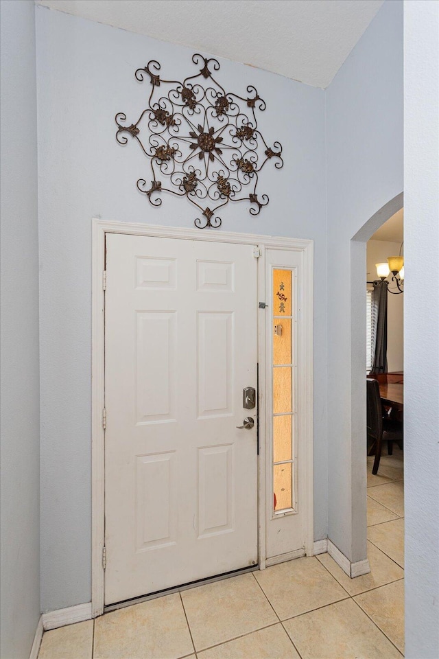 foyer entrance with arched walkways, light tile patterned flooring, and baseboards