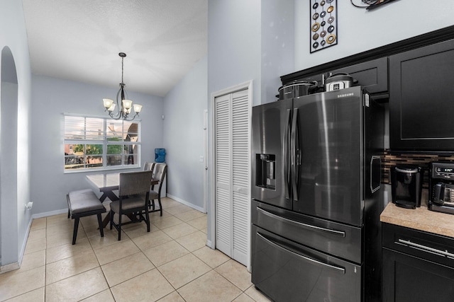 kitchen featuring light tile patterned floors, a notable chandelier, dark cabinets, light countertops, and stainless steel fridge