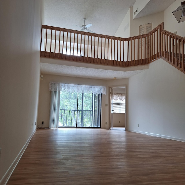 unfurnished living room featuring a towering ceiling, hardwood / wood-style flooring, and ceiling fan