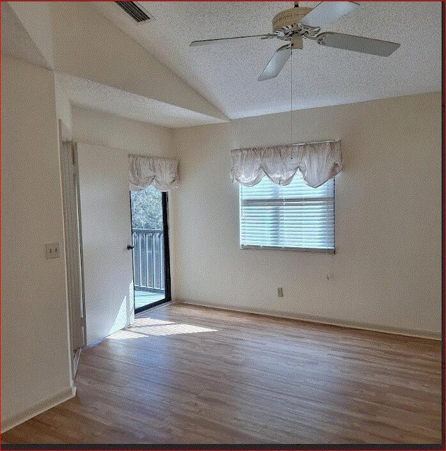 empty room with ceiling fan, lofted ceiling, a textured ceiling, and wood-type flooring