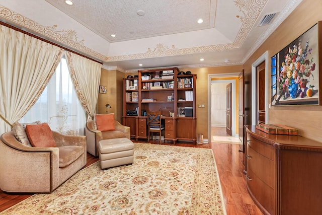 living area with a raised ceiling, ornamental molding, and hardwood / wood-style floors