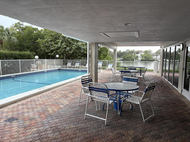 community pool with a patio area, fence, and outdoor dining area