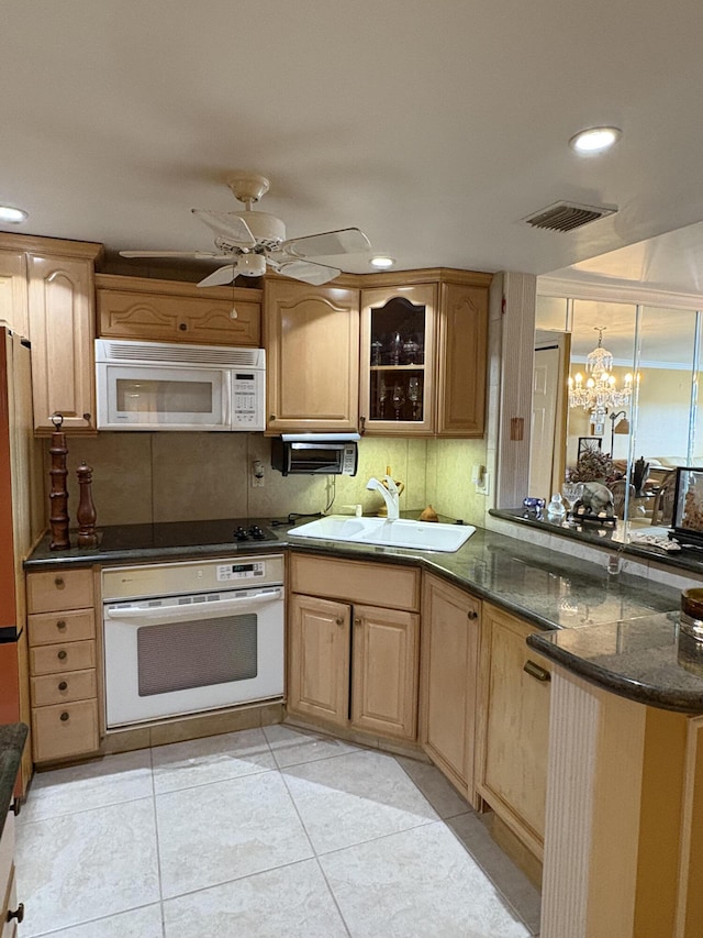 kitchen featuring sink, light tile patterned floors, white appliances, dark stone counters, and ceiling fan with notable chandelier