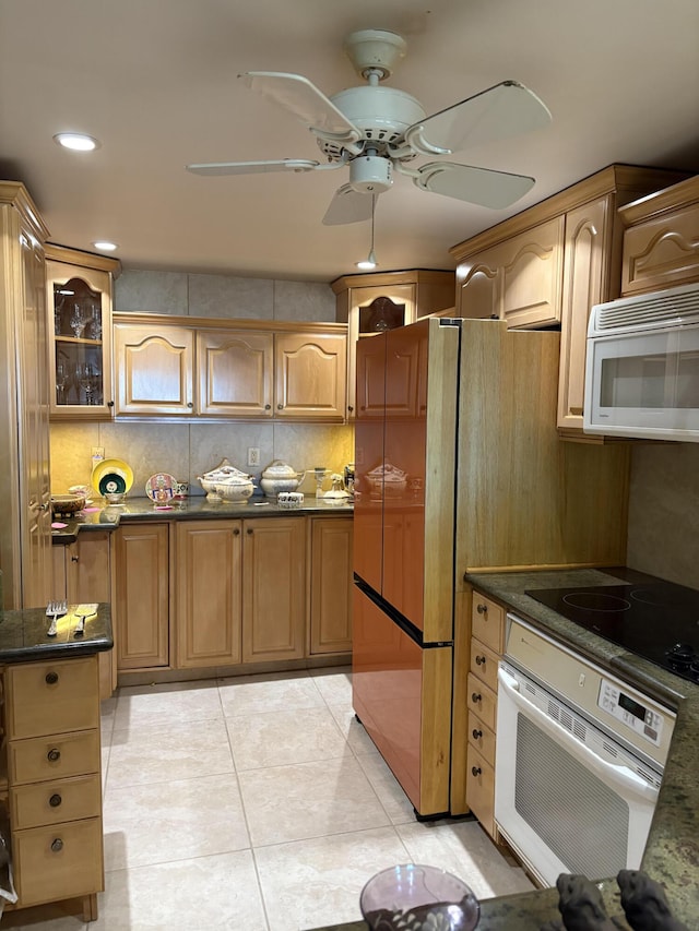 kitchen with light tile patterned floors, white appliances, dark stone counters, and ceiling fan