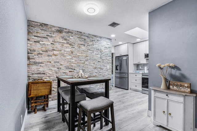 kitchen featuring light hardwood / wood-style flooring, stainless steel appliances, white cabinets, and a skylight