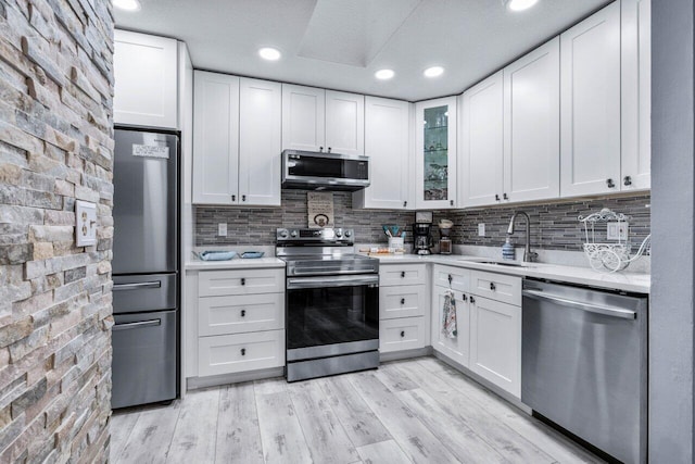 kitchen with stainless steel appliances, backsplash, white cabinets, light hardwood / wood-style flooring, and sink