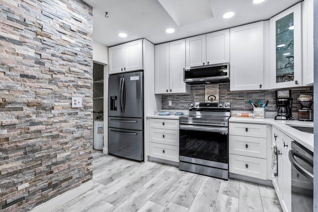 kitchen with appliances with stainless steel finishes, tasteful backsplash, white cabinets, and light hardwood / wood-style floors