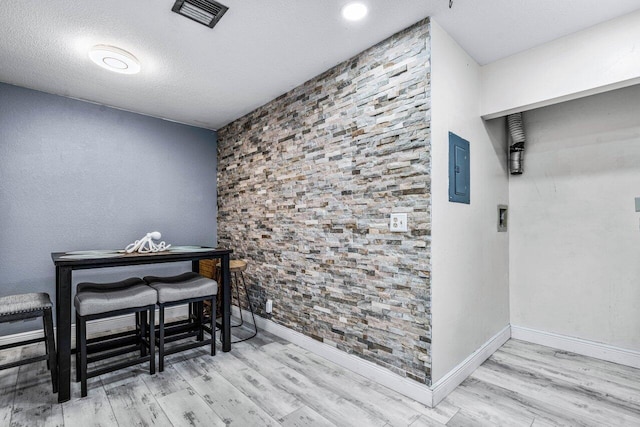 dining area featuring a textured ceiling, electric panel, and light hardwood / wood-style flooring