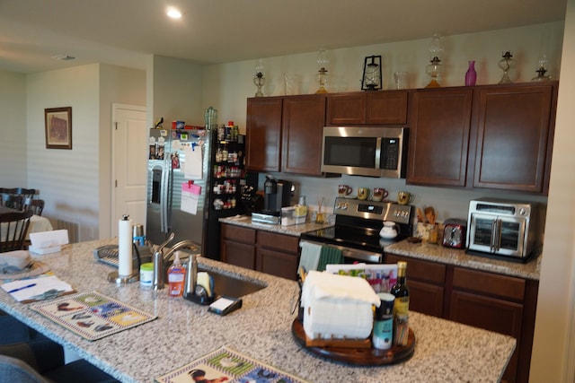 kitchen with a breakfast bar area, dark brown cabinetry, a kitchen island with sink, and appliances with stainless steel finishes