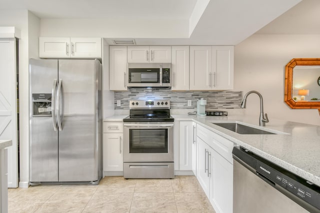 kitchen featuring stainless steel appliances, backsplash, light stone countertops, white cabinets, and sink