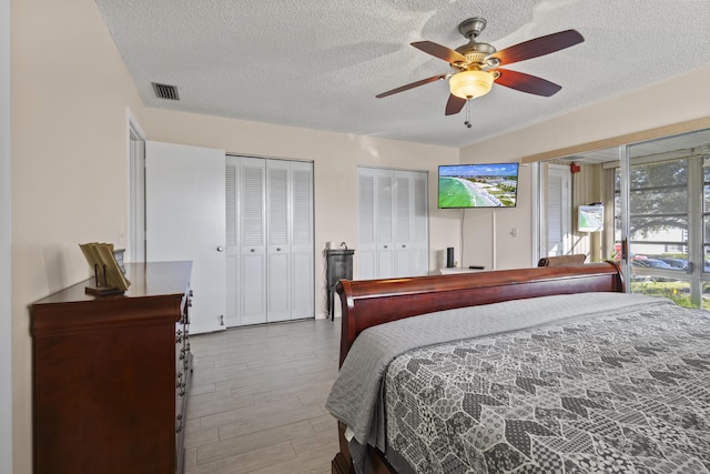 bedroom with multiple closets, light wood-type flooring, a textured ceiling, and ceiling fan