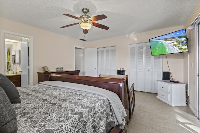 bedroom with ensuite bath, ceiling fan, light hardwood / wood-style floors, a textured ceiling, and two closets