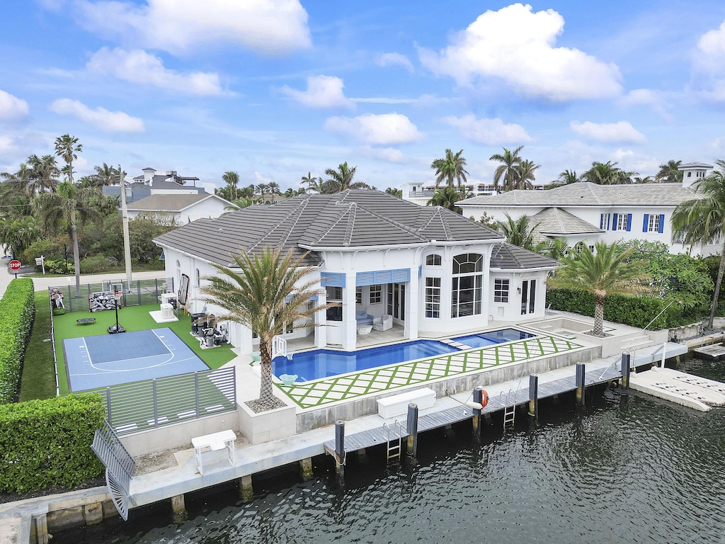 rear view of house featuring a pool with hot tub, a water view, a lawn, and a patio