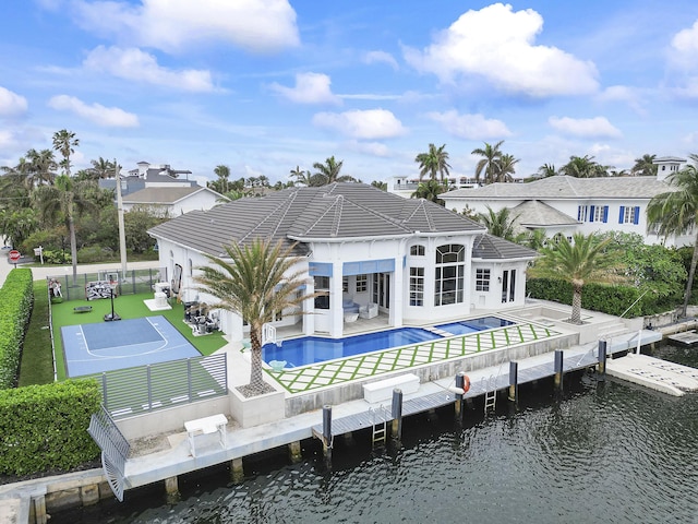 rear view of house featuring a pool with hot tub, a water view, a lawn, and a patio