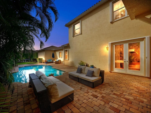 pool at dusk featuring a patio area, french doors, and an outdoor living space