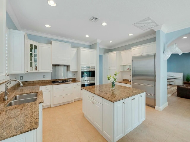 kitchen featuring white cabinets, stainless steel appliances, dark stone counters, a kitchen island, and sink