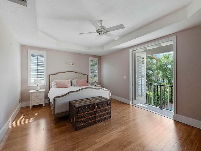 bedroom featuring access to outside, a tray ceiling, multiple windows, and wood finished floors