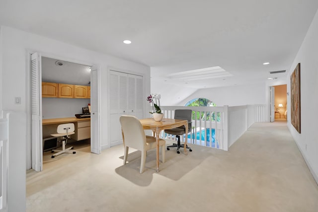 home office featuring light carpet, built in desk, and vaulted ceiling