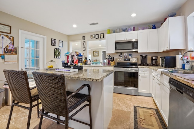 kitchen featuring white cabinetry, sink, a breakfast bar area, light stone counters, and stainless steel appliances