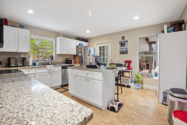 kitchen featuring white cabinetry, light stone counters, stainless steel appliances, and a kitchen island