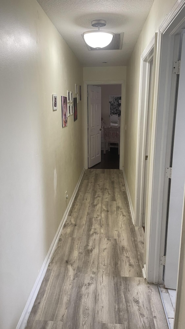 corridor with a textured ceiling and light hardwood / wood-style floors