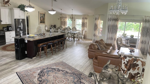 kitchen featuring a kitchen breakfast bar, vaulted ceiling, a kitchen island with sink, appliances with stainless steel finishes, and white cabinets