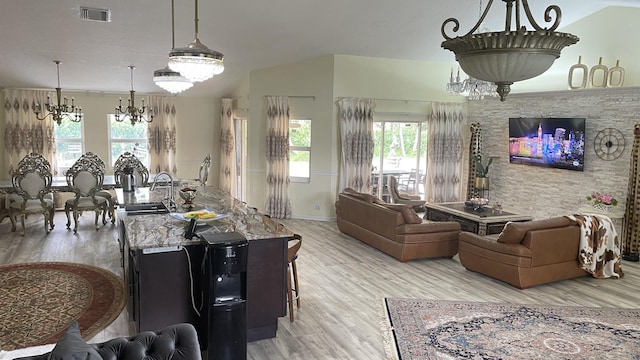 living room with a healthy amount of sunlight, light hardwood / wood-style flooring, an inviting chandelier, and vaulted ceiling