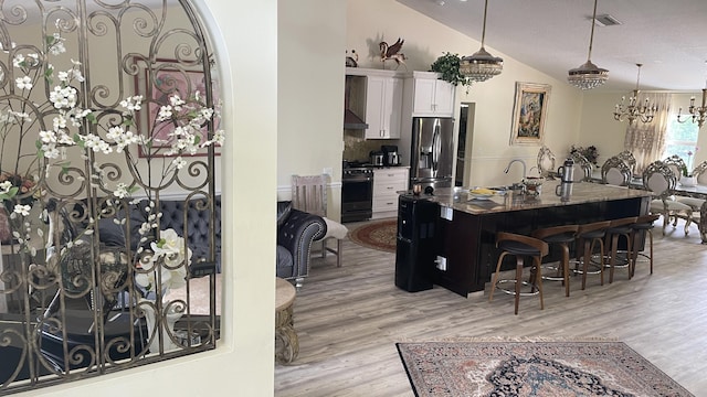 kitchen featuring gas range, vaulted ceiling, stainless steel fridge with ice dispenser, a breakfast bar area, and white cabinets