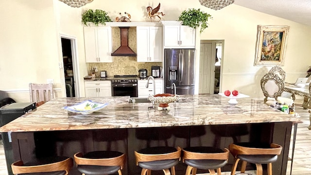 kitchen featuring vaulted ceiling, wall chimney exhaust hood, tasteful backsplash, white cabinets, and appliances with stainless steel finishes